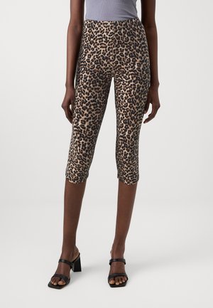 Kvinde-model iført leopardprintet cropped leggings med høj talje og sorte åbne tå-sandaler med blokhæl på ensfarvet baggrund.