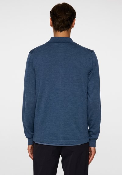 Polo a maniche lunghe di colore blu scuro in maglia, con colletto, caratterizzato da un tessuto testurizzato e polsini a costine, visto da dietro.