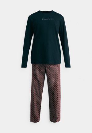 Črna srajca z dolgimi rokavi s logotipom "Calvin Klein" na prsih, v kombinaciji s patterned rdečimi in mornarsko modrimi hlačami z geometrijskimi oblikami.