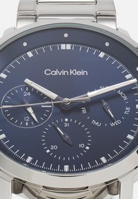 Calvin Klein metallklocka med en mörkblå urtavla, som har timmarkörer i silverfärg, tre subdials och ett armband i rostfritt stål.