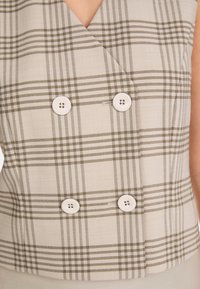 Braun- und cremefarbener Karo-Weste mit doppelt geknöpftem Design, ausgestattet mit vier runden weißen Knöpfen und einer glatten Stoffstruktur.