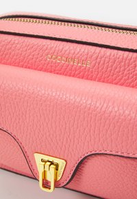 Borsa a tracolla in pelle rosa con finitura strutturata, accessori in oro e chiusura triangolare. Presenta cuciture nere a contrasto e branding impresso.