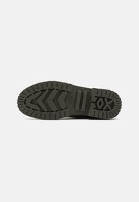 Black rubber shoe sole with a rugged tread pattern, featuring grooves and grips designed for traction and durability.