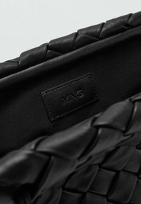 Interno di una borsa in pelle intrecciata nera con una texture liscia e un'etichetta di marca visibile. Presenta una rifinitura intrecciata lungo l'apertura.