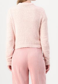 Ljusrosa, strukturerad stickad tröja med långa ärmar och en kortare fåll, ihop med matchande rosa manchesterbyxor. Inga synliga mönster eller detaljer.