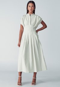 Hellgrünes gestreiftes Midikleid mit Puffärmeln, Knopfleiste vorne und gefälteltem Rock. Kombiniert mit weißen Riemchenschuhen. Glatte Textur.