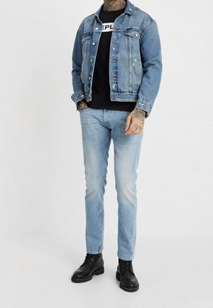 Džínová bunda ve světle modré barvě se zničenými detaily, doladěná s černým tričkem s grafikou, světle modrými džíny a černými botami.