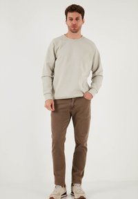 Felpa grigia chiara a girocollo, maniche raglan, abbinata a pantaloni slim-fit marroni. Sneaker con accenti beige e marroni completano l'outfit.