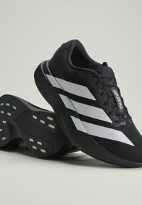 Chaussures de course Adidas Adizero noires avec bandes blanches et semelle épaisse, présentées sur un fond clair uni.