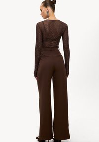 Haut marron à manches longues avec une texture transparente et des clous argentés, associé à un pantalon marron taille haute à jambes larges.