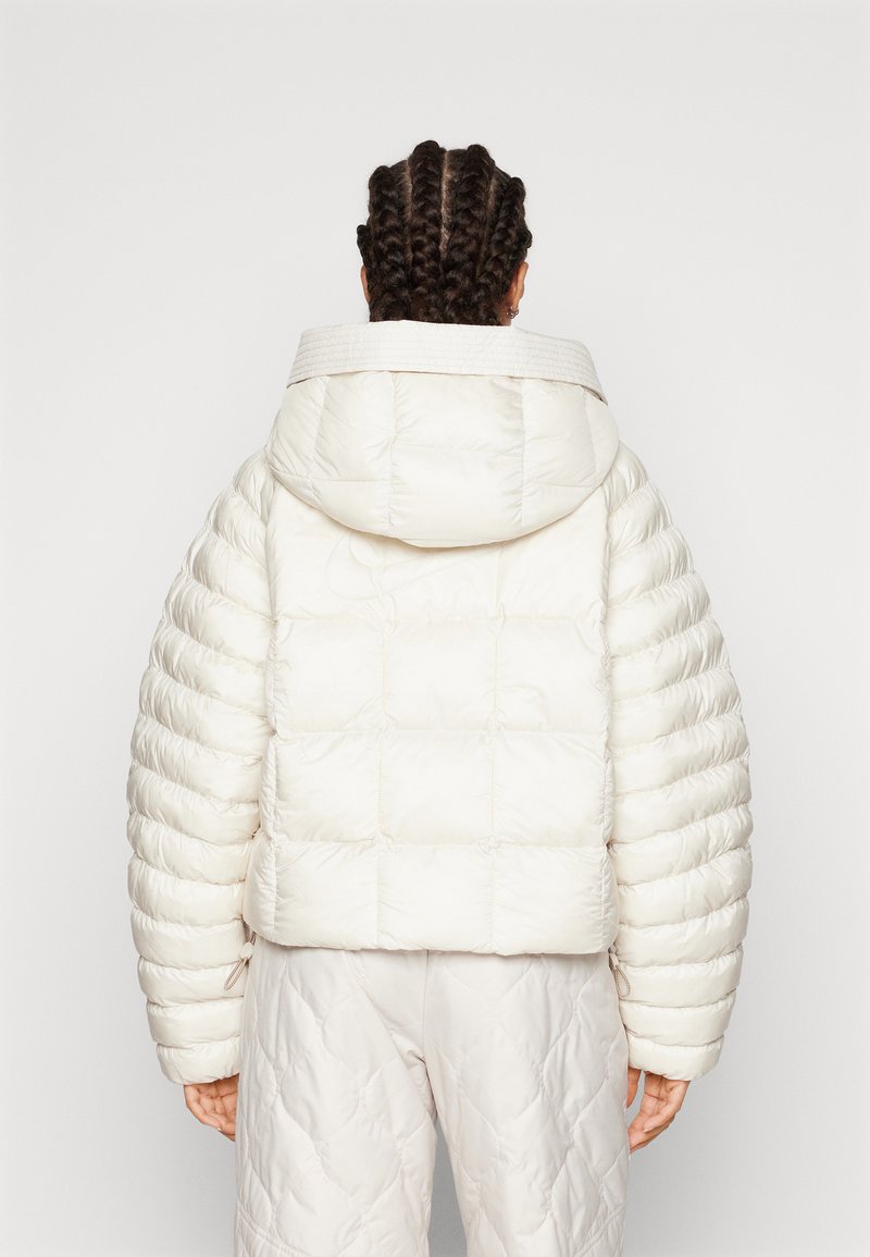 Giubbotto imbottito di colore avorio, con cappuccio, design trapuntato e dettagli a coste sul colletto. Maniche arrotondate e oversize con una texture morbida.