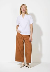 Blouse blanche à manches courtes avec un petit col en V, associée à un pantalon large marron et des sandales de couleur claire. Design simple et fonctionnel.
