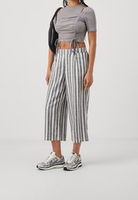 Šedý žebrovaný crop top s bočními výřezy, spárovaný s šedými a bílými pruhovanými širokými kalhotami a metalickými teniskami. Obsahuje černou tašku.