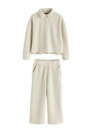 Completo beige a coste composto da due pezzi con polo a maniche lunghe con bottoni e pantaloni a gamba larga con fascia elastica in vita e tasche laterali.
