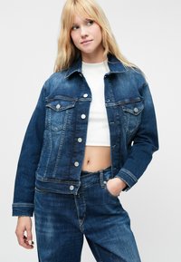 Denim jakna tamnoplave boje sa dugmadi sprijeda, džepovima na prsima i manžetama. Materijal ima teksturirani finiš. Uparena s odgovarajućim trapericama.
