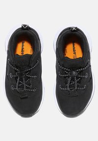 Black athletic shoes with textured fabric upper, elastic laces, and white soles. Orange insoles visible through the openings.