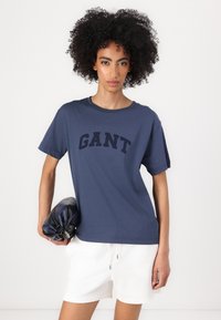 Marineblå kortærmet t-shirt med 'GANT' logo. Fremstillet af bomuld, med rund halsudskæring og afslappet pasform. Sæt sammen med hvide shorts.