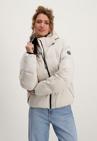 Lichtgewicht gewatteerde jas in crème met een aansluitende capuchon, zwarte rits en elastische manchetten. Bevat een rond logo op de linkermouw.