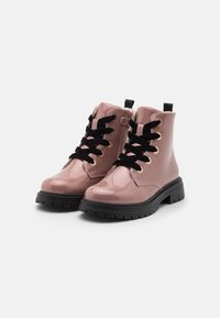 Botas de tobillo de charol rosa con cordones negros y ojales dorados; suela de goma negra gruesa y tira trasera para facilitar el calzado.