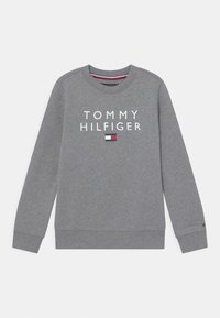 Sweat-shirt gris Tommy Hilfiger avec texte logo blanc et petit emblème en rouge, blanc et bleu à l'avant et sur le poignet.