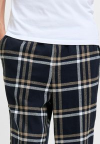 Pantaloni a quadri navy in morbido tessuto con linee bianche e beige. Presentano una vestibilità comoda e tasche laterali.
