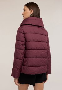 Giubbotto imbottito borgogna con ampio colletto, design trapuntato e maniche lunghe. Materiale leggero con una texture liscia, vestibilità corta.