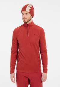Pullover in pile rosso con colletto alto, zip a un quarto e dettaglio del logo. Indossato con un berretto abbinato rosso con una striscia bianca e logo.