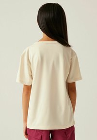 Camiseta beige de manga corta con escote redondeado, textura suave y detalles de costura sutil, vista desde la parte posterior.