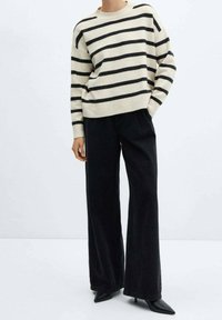 Sweter w paski w kolorze kremowym z czarnymi paskami, połączony z czarnymi dżinsami o wysokim stanie i szerokich nogawkach. Teksturowana dzianina, luźny krój, długie rękawy.