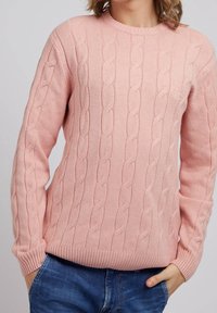 Hellrosa, aus Kabelstrick gefertiger Pullover mit Rundhalsausschnitt sowie gerippten Bündchen und Saum. Verfügt über dezentes Branding auf der Brust. Getragen mit blauen Jeans.
