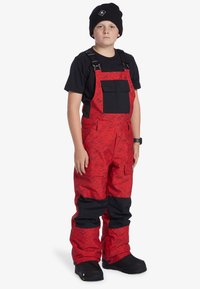 Röda och svarta snöoveraller gjorda av ett hållbart, vattenavvisande material, med en framficka och justerbara remmar. Svarta kängor ingår.