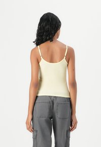 Yellow ribbed tank top with thin straps, featuring adjustable hardware, paired with grey cargo pants with large back pockets.