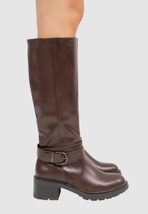Bottes marron hautes jusqu'au genou en cuir lisse, avec un large revers, une boucle au niveau de la cheville et un talon épais pour plus de stabilité.