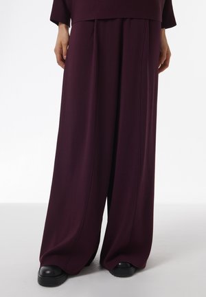 Wide-leg pants in deep burgundy fabric, featuring front pleats and a loose silhouette, paired with chunky black shoes.