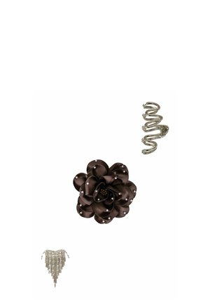 Broche de flor de tela negra con pequeñas perlas, anillo espiral de plata y joyería con cadena de flecos plateada sobre un fondo blanco.