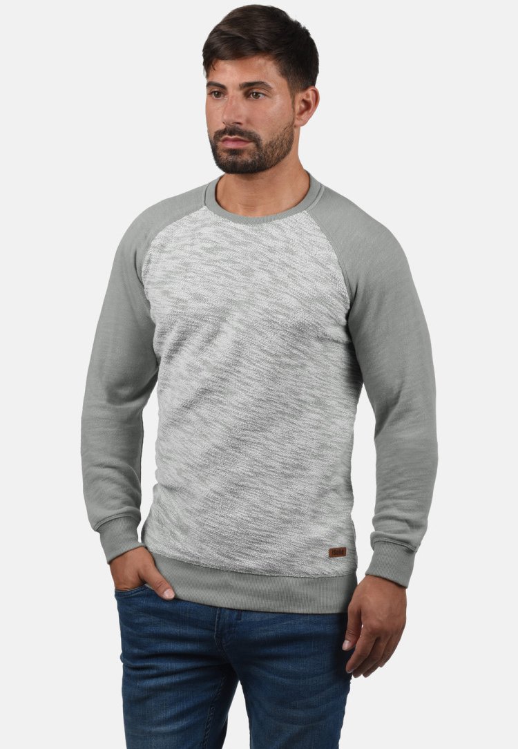 Sudadera gris claro con una parte delantera texturizada y mangas grises lisas. Presenta puños y bajo acanalados, con un pequeño logo de marca cerca de la parte inferior.