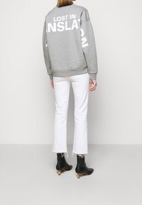 Sudadera gris con un gran texto blanco "PERDIDO EN LA TRADUCCIÓN" en la espalda, combinada con vaqueros blancos acampanados y botas negras de tacón de madera hasta el tobillo.