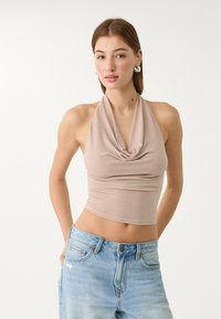 Beige halterneck croptop med draperad front, tillverkad av elastisk, texturerad tyg, kombinerat med högmidjade ljusblå jeans.