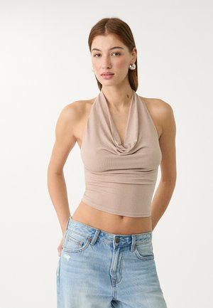 Top court à col halter beige avec une partie drapée à l'avant, fabriqué en tissu extensible et texturé, associé à un jean taille haute bleu clair.