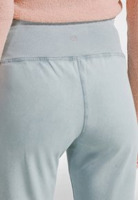Primer plano de una persona que lleva pantalones de cintura alta de color azul claro con cintura acanalada y un suéter peludo rosa claro.