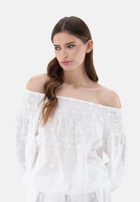 Weißes Off-Shoulder-Blusenshirt mit floralen Stickereien, gerafftem Ausschnitt und lockerer Passform. Weicher, leichter Stoff mit zarten Details.