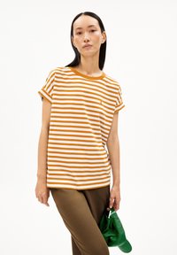 Striped t-shirt in white and burnt orange, featuring a round neckline, rolled sleeves, and a small logo; paired with olive green pants.