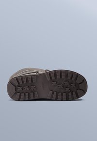 Semelle de botte présentant un design en caoutchouc texturé de couleur brun foncé avec des motifs de crampons profonds pour une meilleure adhérence. Caractérisée par un bord renforcé et une surface lisse.