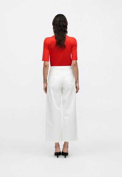 Κόκκινο εφαρμοστό πουκάμισο με κοντά μανίκια συνδυασμένο με λευκό παντελόνι ψηλόμεσο, φαρδύ, με καθαρό κόψιμο και μπροστινές τσέπες.