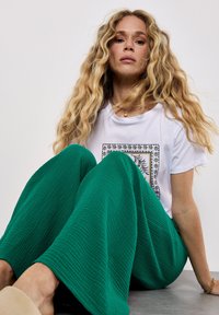 Witte t-shirt met een patroon, gecombineerd met brede groene textuurbroek. De outfit heeft een losse pasvorm en een casual ontwerp.