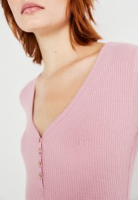 Rosa ribbet stoff top med dyp V-hals, med en liten brodert "Lee" logo og seks knapper langs fronten.