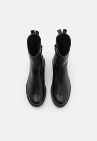 Bottines en cuir noir avec une texture lisse, bout rond et fermeture à glissière de chaque côté. Présentent un talon court et des languettes de tirage.