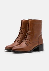 Bottes chelsea en cuir marron avec un design épuré, bouts pointus, lacets à l'avant et un petit talon carré. Surface texturée avec des coutures minimales.