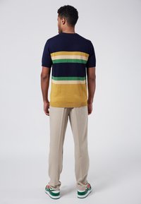 Suéter de punto de manga corta con rayas horizontales en azul marino, amarillo, verde y crema, combinado con pantalones beiges y zapatos con acentos verdes.