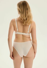 Biustonosz i majtki w miękkim, białym materiale. Posiada regulowane ramiączka, złote akcenty i gładki, bezszwowy design.